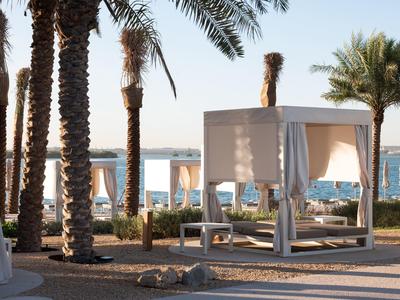 Strand mit Palmen und weißen Tagesbetten, blauer Himmel und Meer im Hintergrund bei Sonnenuntergang.