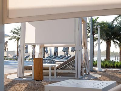 Zwembadgebied met witte ligbedden en cabana's, omgeven door palmbomen op een vakantieplek.