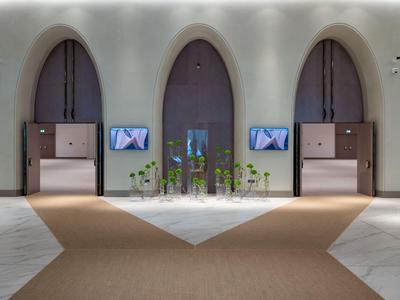 Drie grote bogenvormige deuren in een modern hotelinterieur met tapijt en schermen.