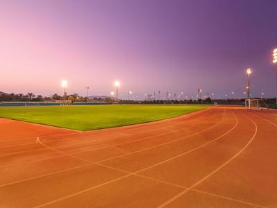 Leeg sportveld met atletiekbaan bij zonsondergang onder paarse lucht.