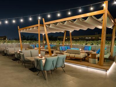 Gezellig buitenterras met verlichte zithoeken en pergola in een hotelomgeving 's nachts.