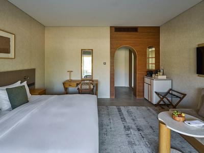 Modernes Hotelzimmer mit großem Bett, Schreibtisch, TV, Stuhl und heller, neutraler Einrichtung.