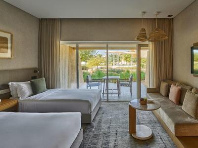 Modernes Hotelzimmer mit zwei Betten, Sofa, Teppich und Blick auf Terrasse mit Garten.