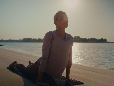 Persoon doet yoga op een rustig strand met zonlicht op de achtergrond