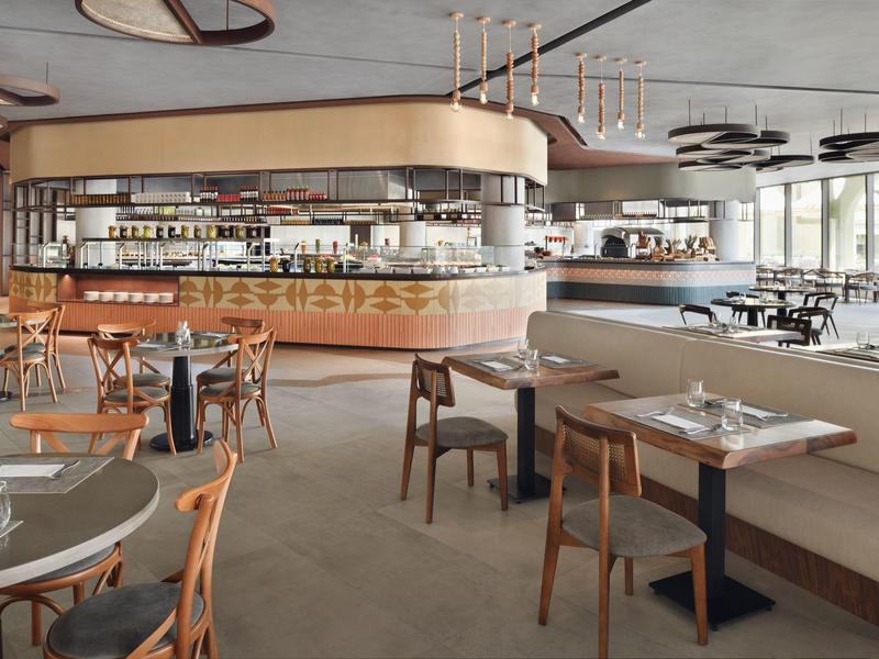 Modernes Restaurant mit Holzstühlen, grauen Tischen und einer runden Bar in hellem Ambiente.