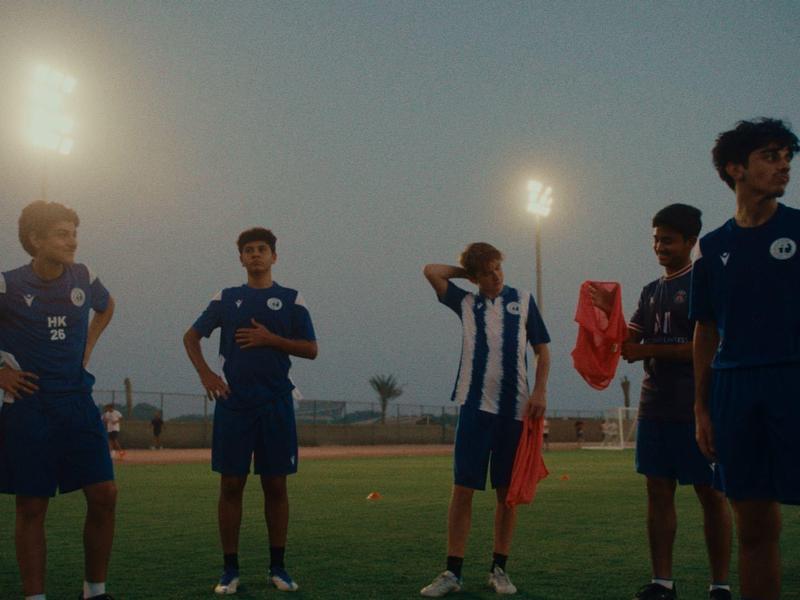 Fünf Jugendliche in Sportkleidung stehen auf einem Fußballfeld bei Dämmerung unter Flutlicht.