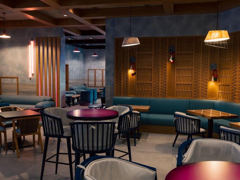 Moderne Café mit dunkelroten Tischen, blauen Sitzen und Holzdecken mit Deckenlampen.