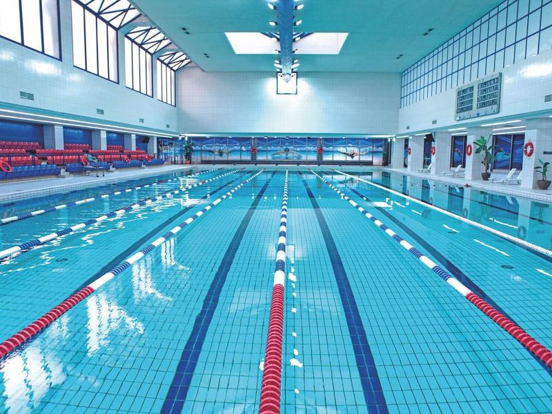 Hallenbad mit sechs Schwimmbahnen, blauen Fliesen und roten Startmarkierungen an den Bahnen.