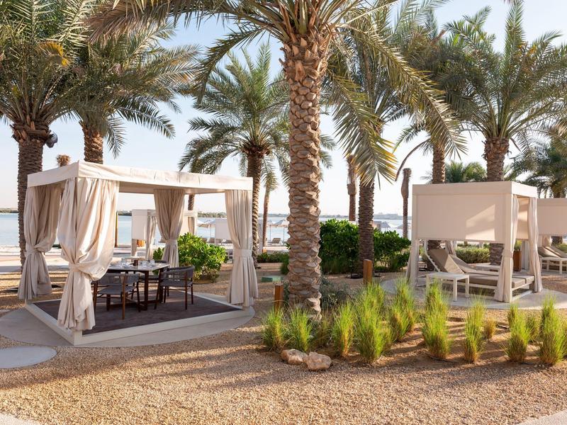 Strand mit Palmen, Holzterrassen und weißen Überdachungen für gemütliche Sitzbereiche.