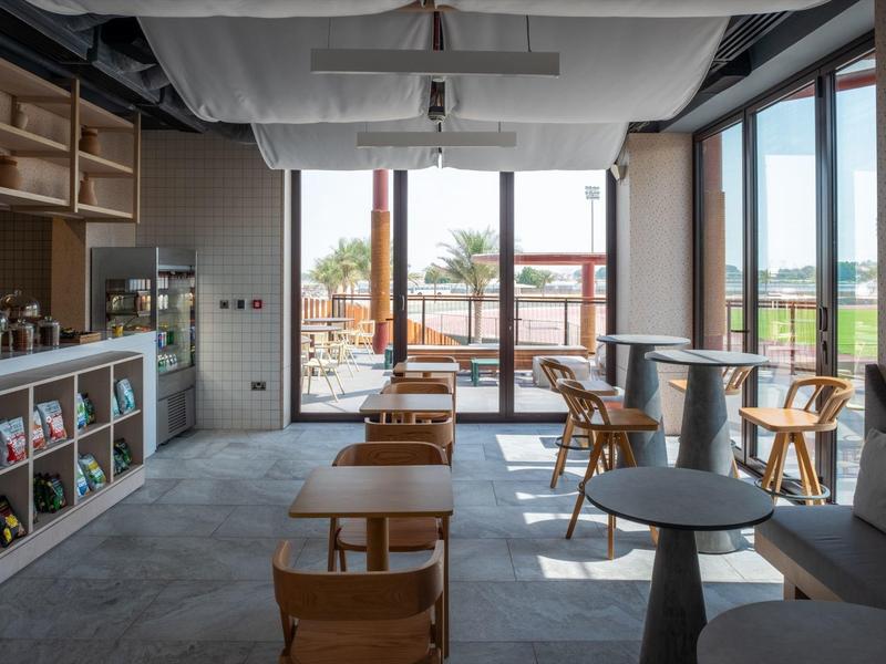 Modernes Café mit Holzstühlen, grauen Tischen, großen Fenstern und Blick auf Terrasse.