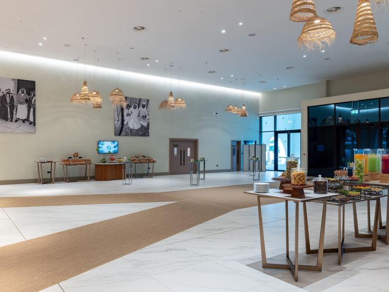 Großer, heller Raum mit weißen Wänden, modernen Lampen und Tischen mit Buffet und Getränken.