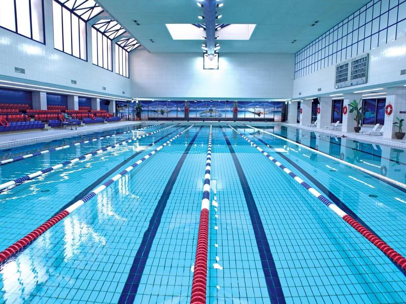 Helles Hallenbad mit klaren blauen Wasser, Bahnseilen und hohen Fenstern an der Decke.