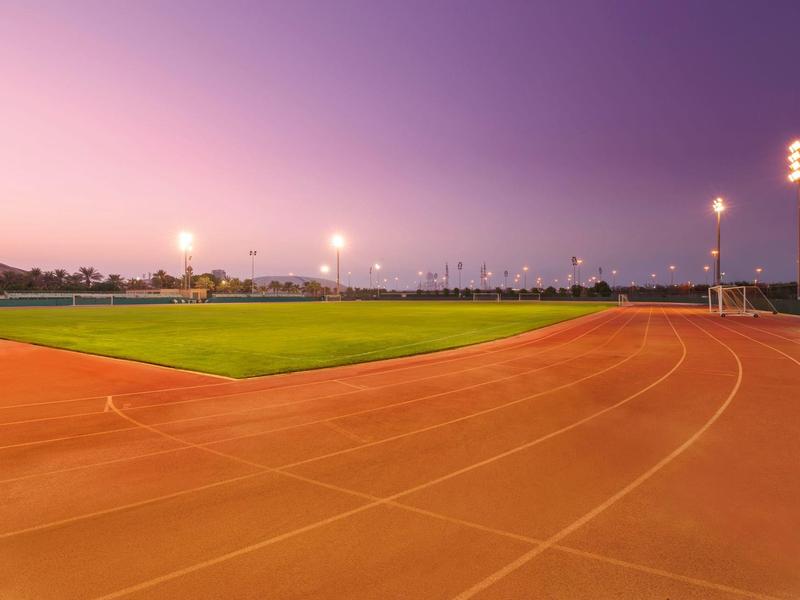 Leerer Sportplatz mit Laufbahn und grünem Spielfeld bei Abenddämmerung und klar lila Himmel.