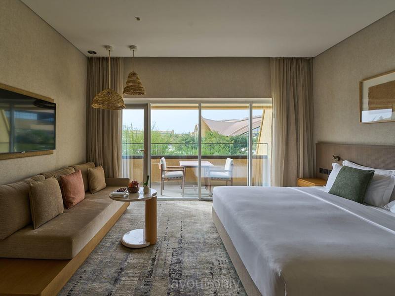 Modernes Hotelzimmer mit großem Bett, Sofa, Teppich und Blick auf den Balkon mit grüner Landschaft.