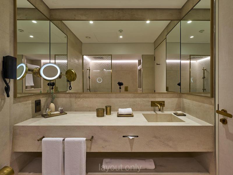 Moderner Badezimmerwaschtisch mit großem Spiegel, goldfarbenen Armaturen und weißen Handtüchern.