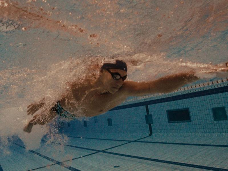 Ein Schwimmer im Becken, Tauchen und Schwimmen unter Wasser mit blauen Fliesen am Boden.