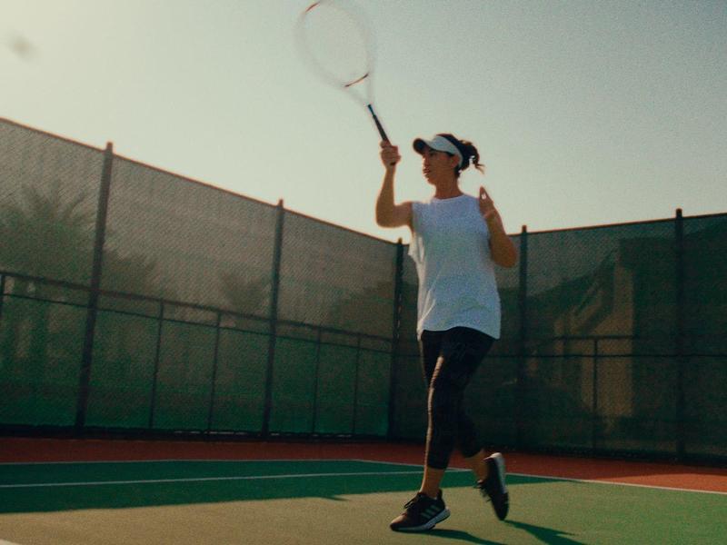 Ein Mann spielt Tennis draußen auf einem Sonnplatz, trägt weiße Kleidung und hält einen Schläger.