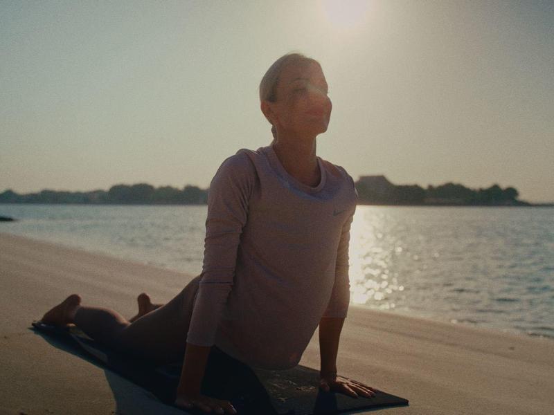 Person macht Yoga am Wasserufer bei Sonnenuntergang mit ruhigem Himmel und spiegelndem Wasser.