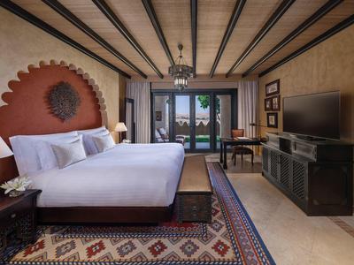 Hotel room with double bed, wooden beams, patterned rug, and balcony view.