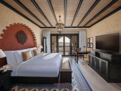 Elegant hotel room with large bed, decorative headboard, balcony, and TV unit.