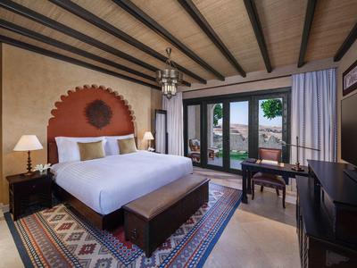 Cozy hotel room with large bed, decorative rug, wooden ceiling beams, and outdoor view.