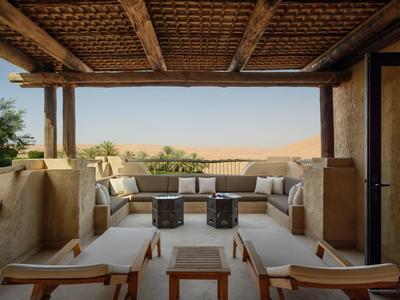 Cozy outdoor lounge with cushioned seats and wooden ceiling overlooking a desert landscape.