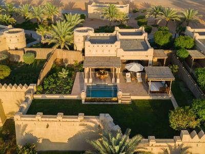 Aerial view of a desert-style hotel with a pool, palm trees, and sandy surroundings.