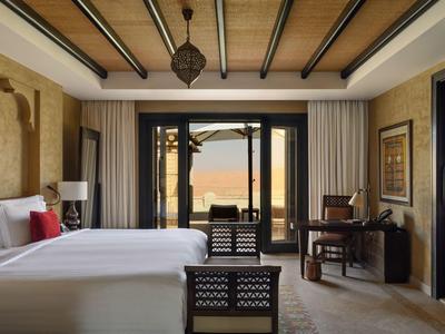 Cozy hotel room with large bed, wooden ceiling, and balcony overlooking a terrace and sea.