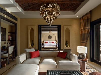 Luxury living room with beige sofa, red cushions, ornate chandelier, and large mirror in a hotel suite.