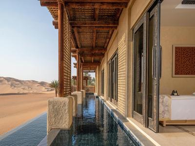 Luxury outdoor pool next to desert-facing hotel room with open doors and wooden ceiling.