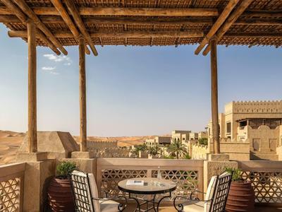 Cozy desert terrace with wrought iron table and chairs under a bamboo roof with scenic view.