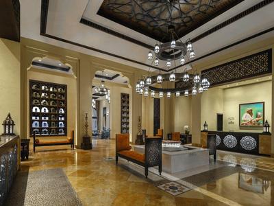 Luxurious hotel lobby with elegant chairs, chandeliers, and decorative ceiling design.