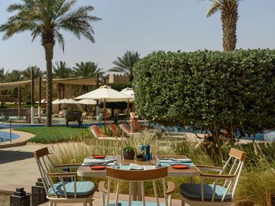 Tavolo con sedie e ombrellone vicino alla piscina in un giardino con palme.