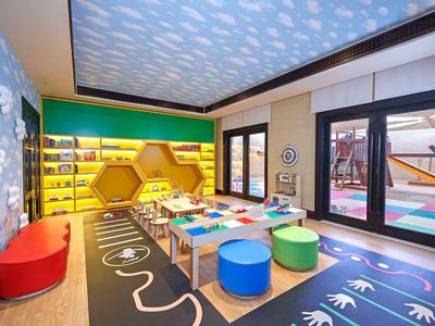 Colorful kids' playroom with hexagonal shelves, cushions, and large windows to outdoor play area.