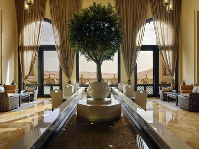 Luxurious hotel lobby with tall windows, elegant curtains, a central tree, and comfortable seating.