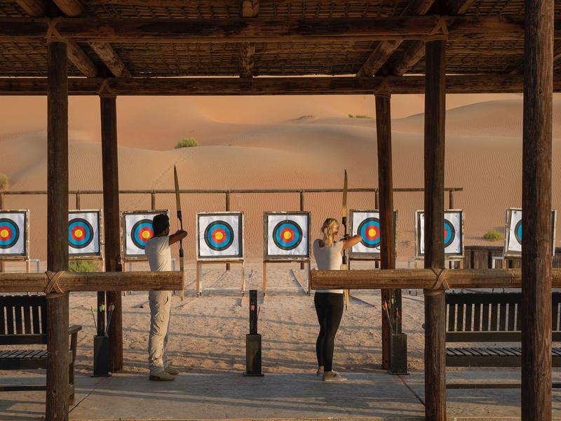Person practicing archery at a rustic outdoor range with wooden targets at sunset.