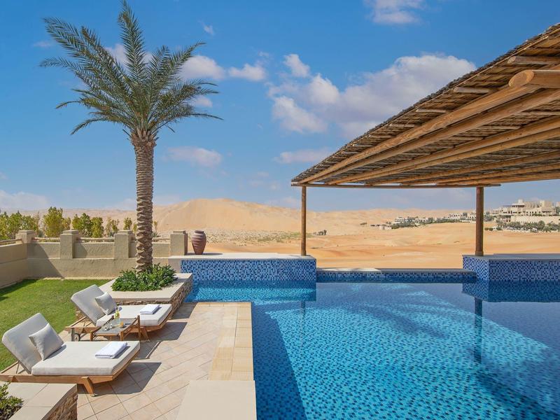 Outdoor pool with lounge chairs and palm tree under blue sky in desert setting