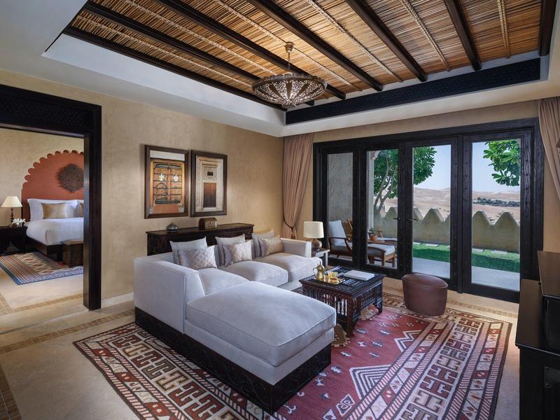 Cozy living room with white sofas, wooden ceiling, large mirror, and glass doors to a garden.