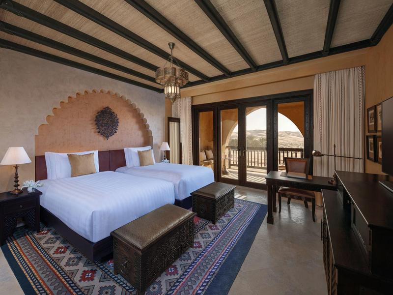 Cozy hotel room with twin beds, wooden beams, a balcony, and traditional decor.