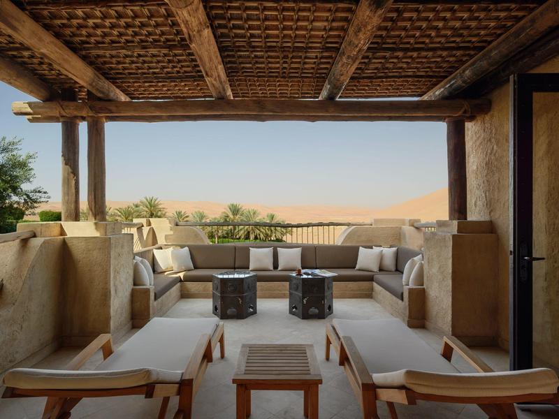 Cozy outdoor lounge with cushioned seats and wooden ceiling overlooking a desert landscape.