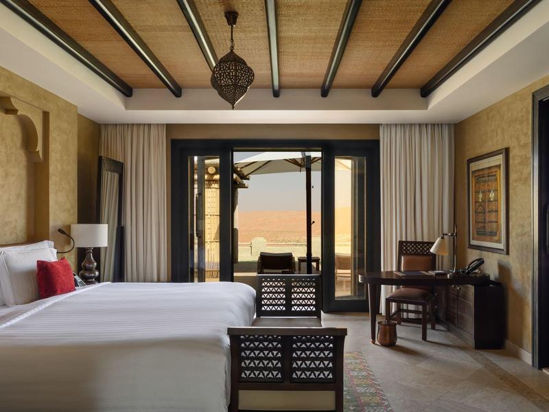 Cozy hotel room with large bed, wooden ceiling, and balcony overlooking a terrace and sea.