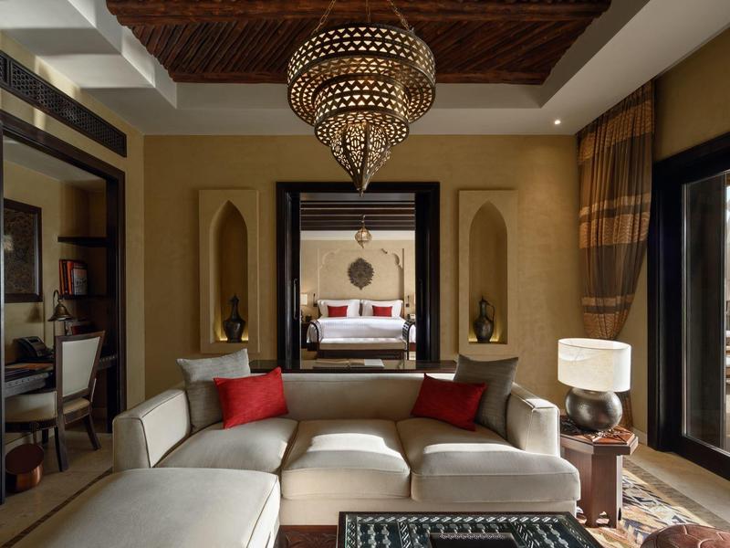 Luxury living room with beige sofa, red cushions, ornate chandelier, and large mirror in a hotel suite.