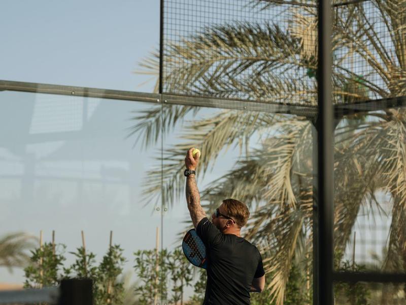 Four people meditate on cushions facing a desert view with clear sky and distant dunes.