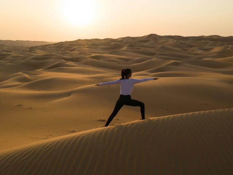 Person doing yoga on sand dunes at sunset in a vast desert landscape.