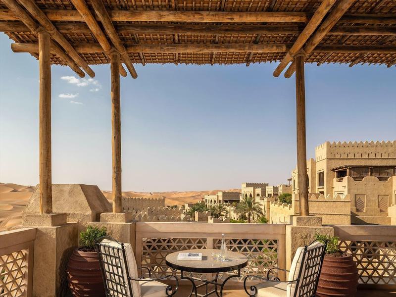 Cozy desert terrace with wrought iron table and chairs under a bamboo roof with scenic view.