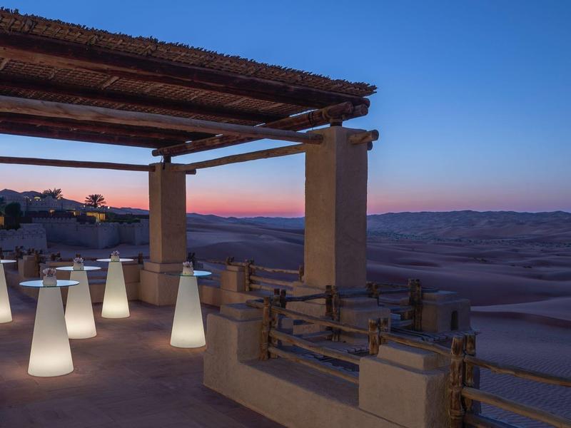 Outdoor terrace with illuminated modern lamps overlooking a desert landscape during sunset.
