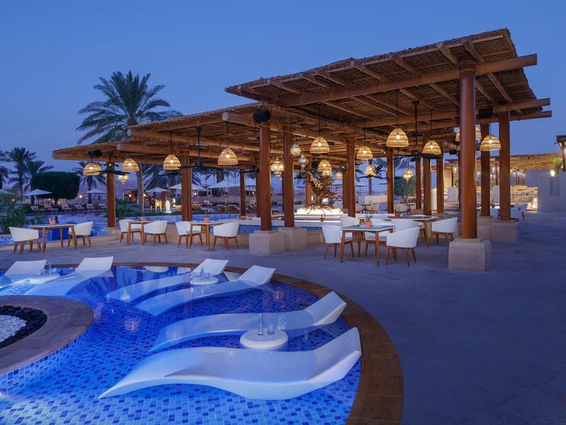 Luxurious pool area with sun loungers next to a hotel on a sandy beach.