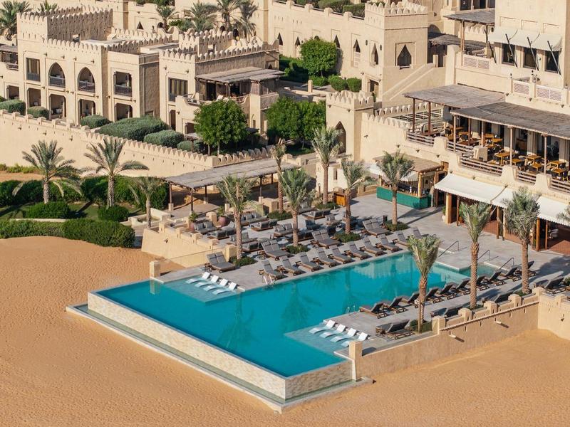Luxurious pool area with sun loungers next to a hotel on a sandy beach.