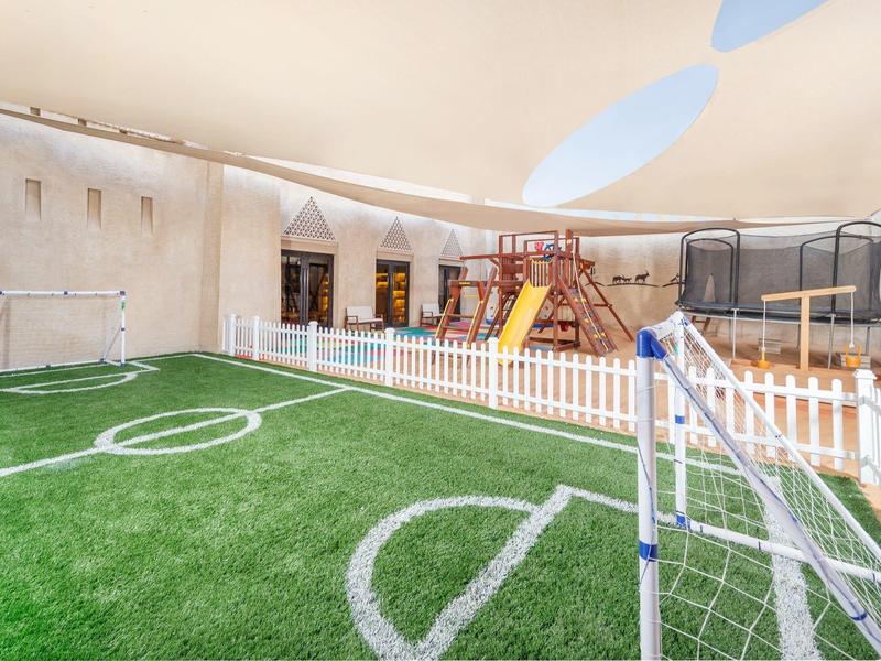 Indoor playground with artificial turf, goalposts, swings, slide, and white fencing under a canopy.