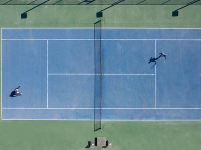 Deux joueurs jouent au tennis sur un court extérieur bleu vus du dessus.